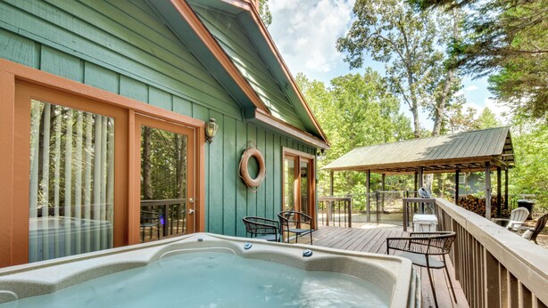 A hot tub on a wooden deck with a covered seating area and a view of trees.