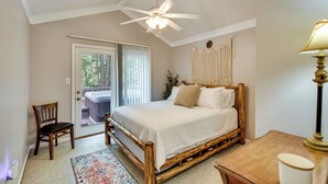 A bedroom with a wooden bed, a ceiling fan, a nightstand, and a view of a hot tub through a sliding glass door.