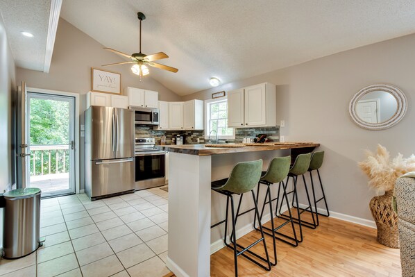 A modern kitchen with stainless steel appliances, a bar area with stools, and a view to the outside. - Dock & Hot Tub at Fair Play Hideaway! (Fair Play)