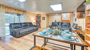 Ein gemütliches Wohnzimmer mit zwei Ledersofas, einem Holzesstisch gedeckt mit blauen Tellern und Gläsern, und einem Bücherregal mit verschiedenen Gegenständen.