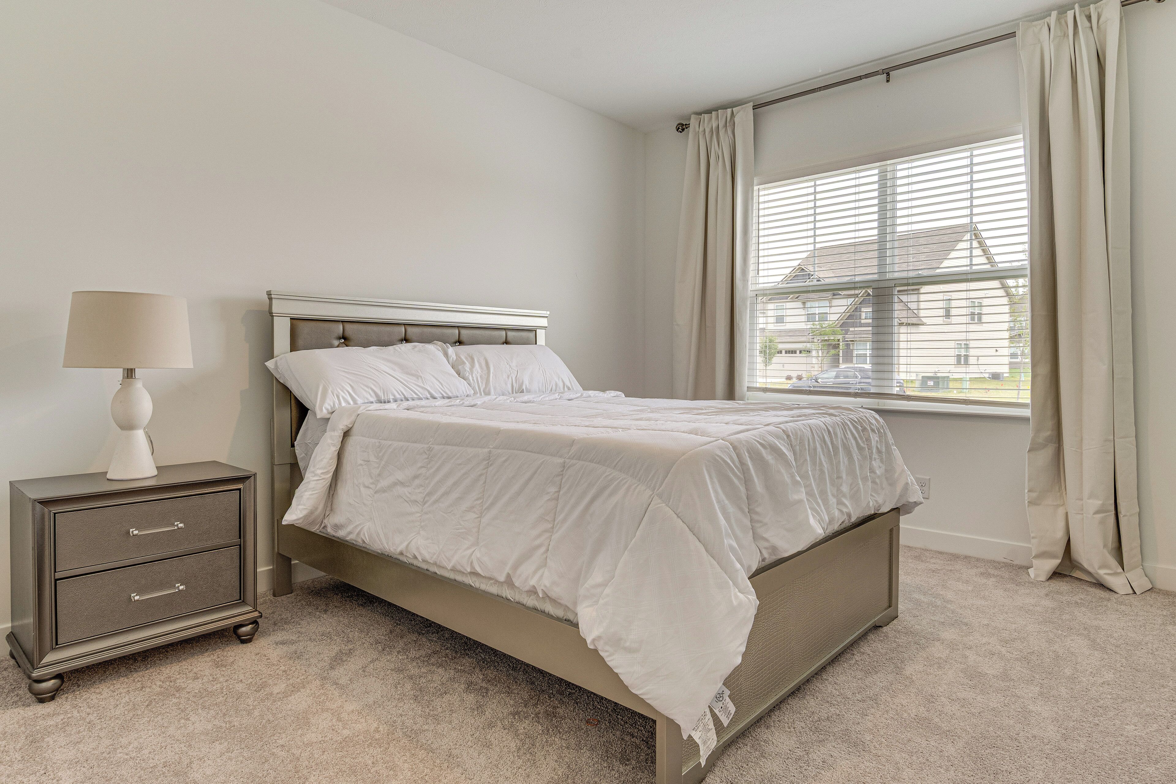 A bedroom with a bed, a nightstand, a lamp, and a window with curtains.