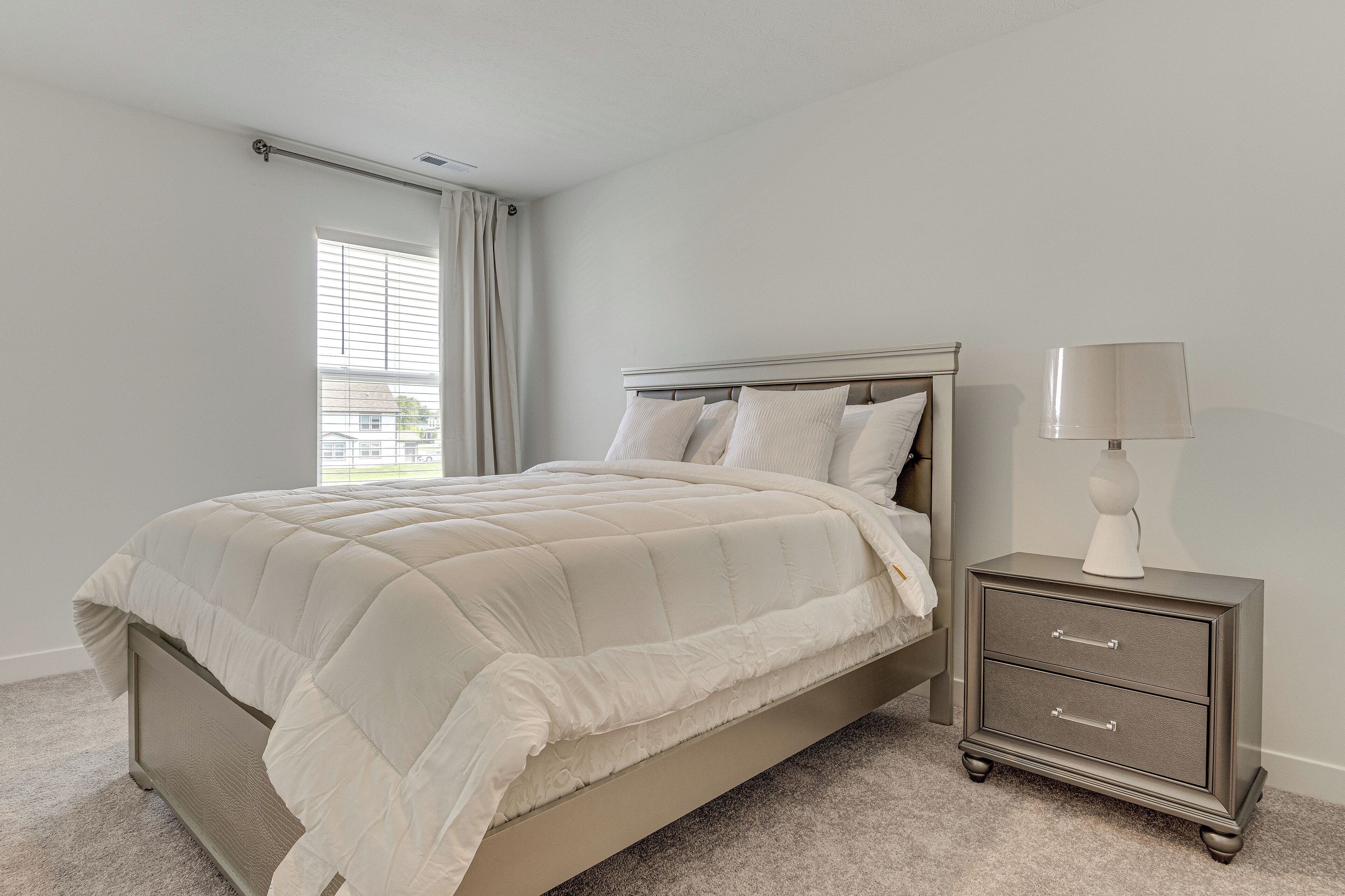 A bedroom with a bed, a nightstand with drawers, and a lamp.