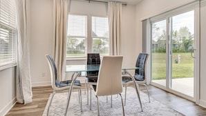 Un comedor moderno con una mesa y sillas de vidrio, ventanas amplias y vistas al exterior.