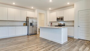 Una cocina moderna con armarios blancos, un refrigerador de acero inoxidable, un microondas y piso de madera.