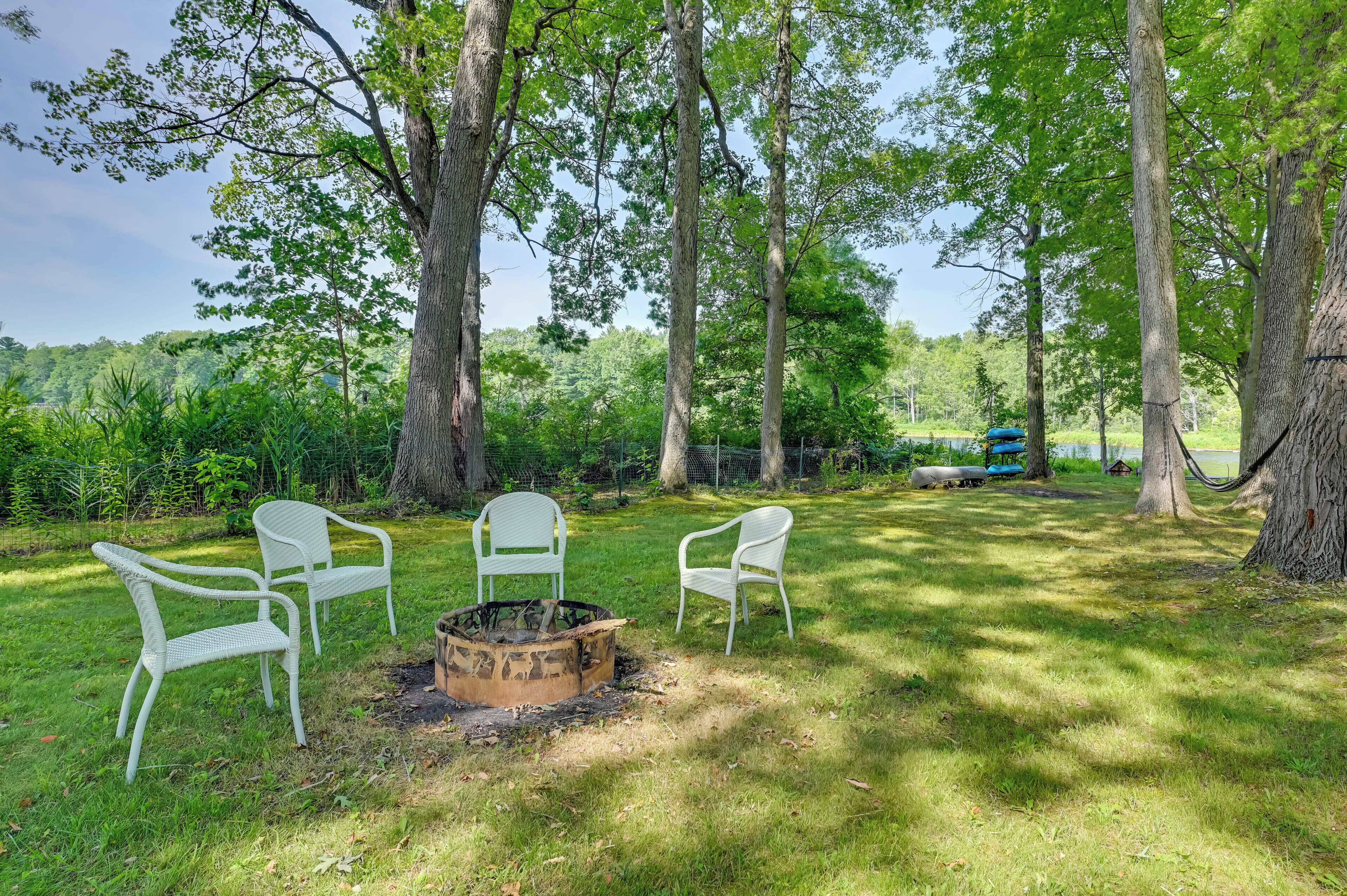 A grassy outdoor area with three white chairs arranged around a fire pit.