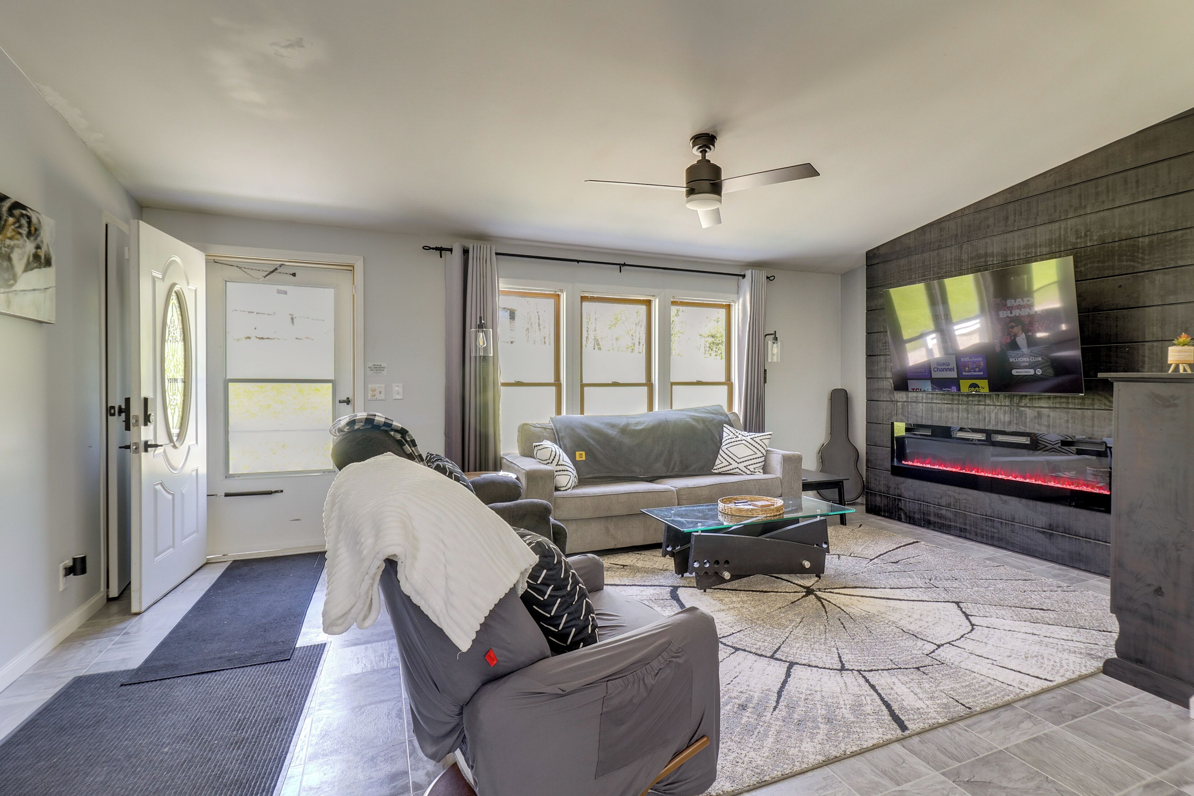 A living room with a sofa, a coffee table, a fireplace, a television, and a ceiling fan.