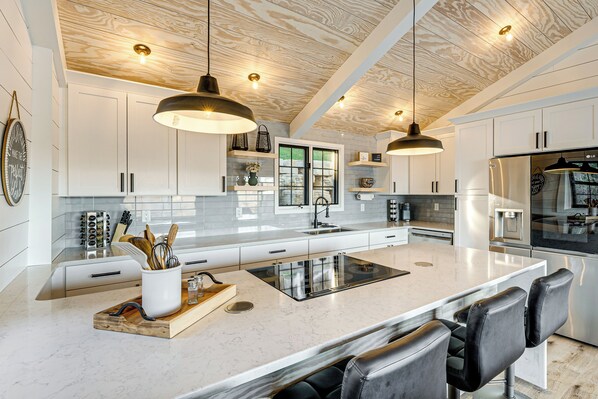 A modern kitchen with white cabinets, a large island with seating, pendant lighting, and stainless steel appliances. - Canoes & Dock: Waterfront Retreat on Lake Beulah! (East Troy)
