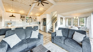 A spacious living area with two grey sofas, a wooden ceiling, and a kitchen in the background. - Canoes & Dock: Waterfront Retreat on Lake Beulah! (East Troy)