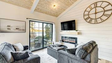 A modern living room with a large wall clock, a fireplace, and a large window overlooking a scenic view.