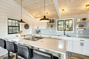 A modern kitchen with a large island, white cabinetry, and pendant lighting. - Canoes & Dock: Waterfront Retreat on Lake Beulah! (East Troy)