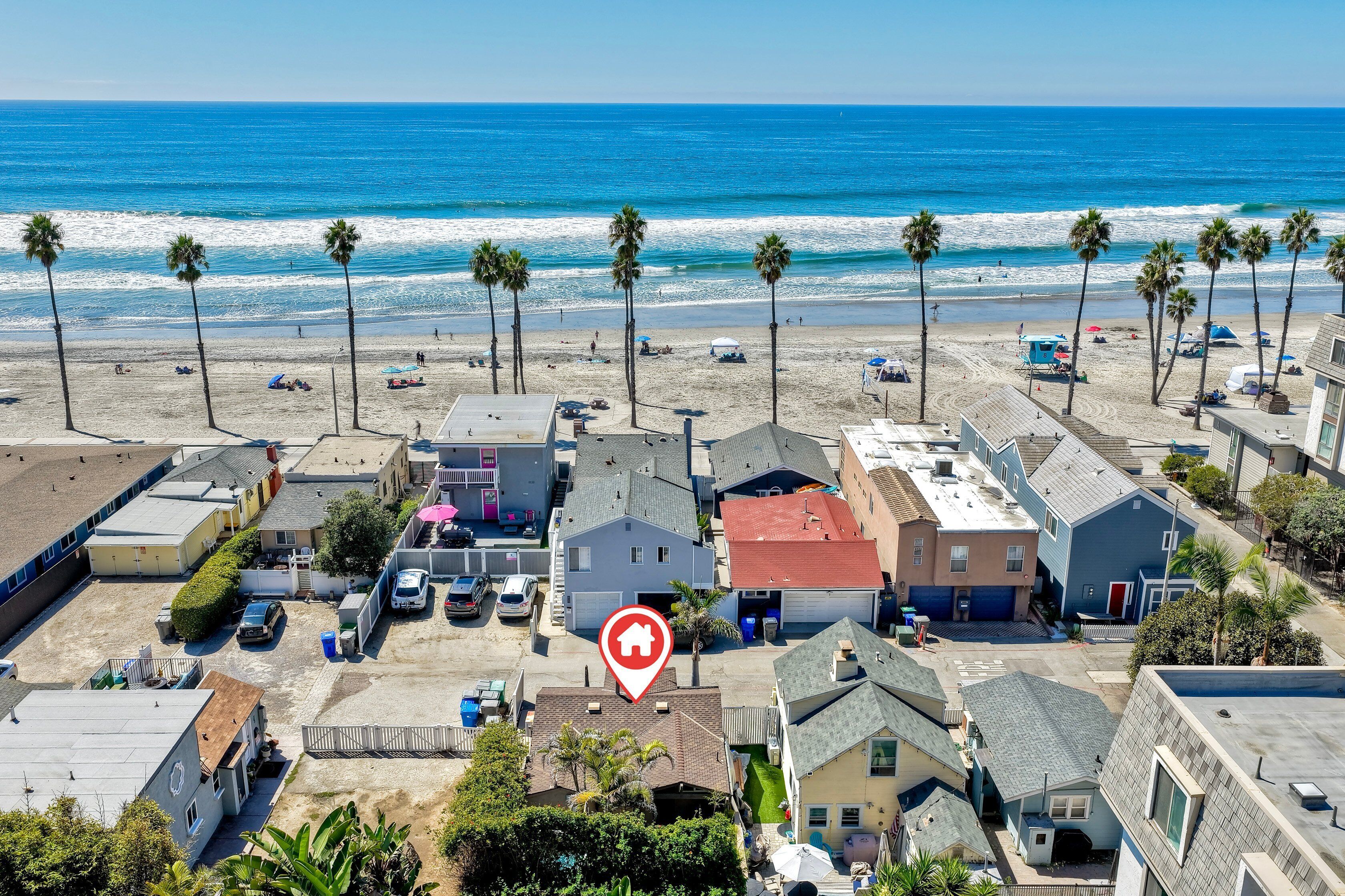 An aerial view of a coastal residential area with houses, a beach, and palm trees.
