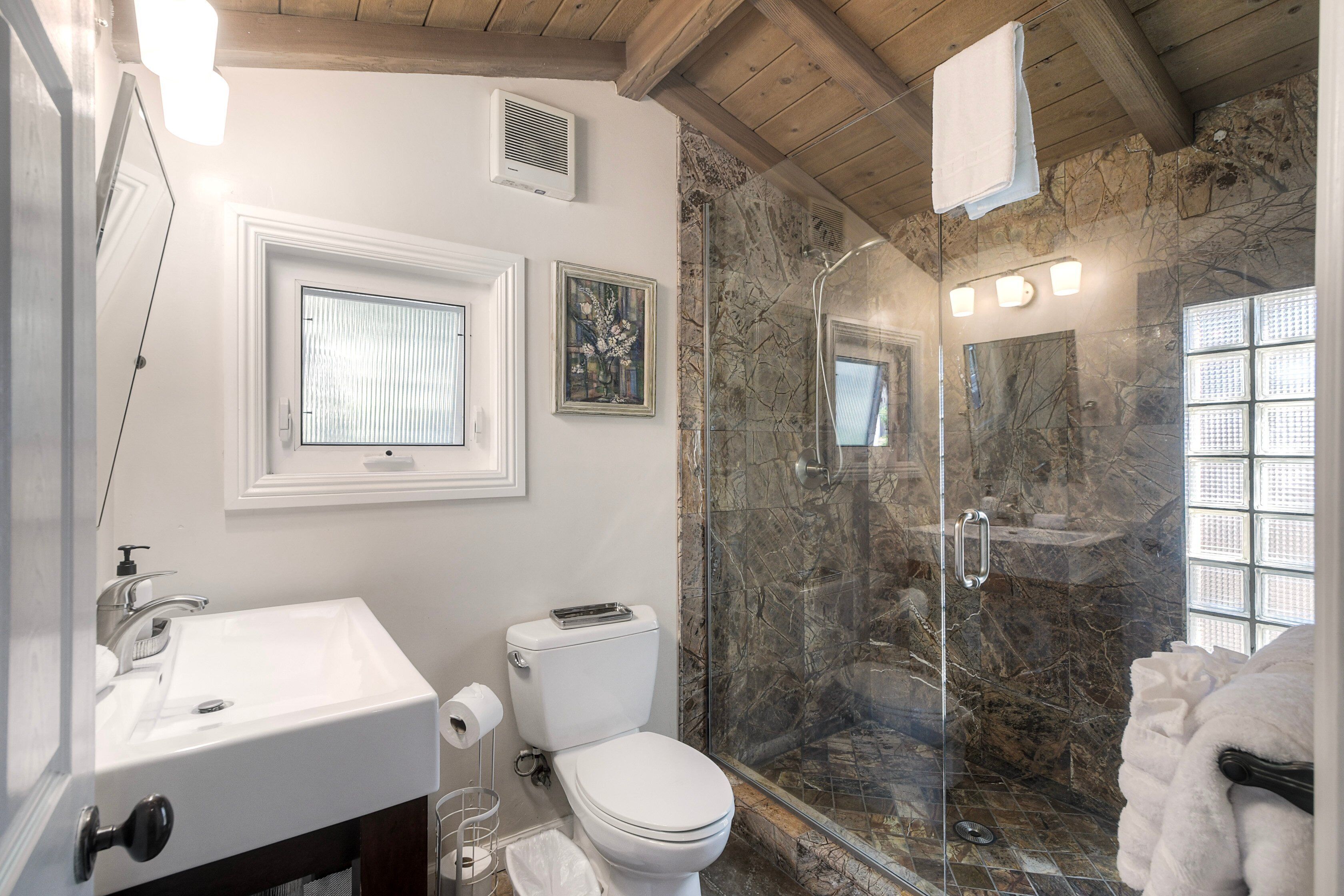 A bathroom with a white sink, toilet, and glass-enclosed shower.