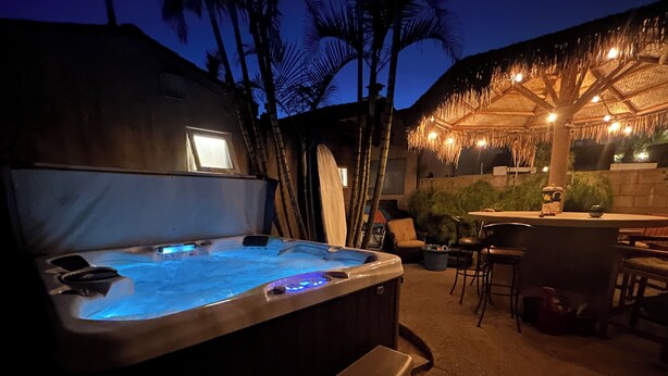 Un jacuzzi con escalones, un área de bar con sillas y una estructura de techo de paja.