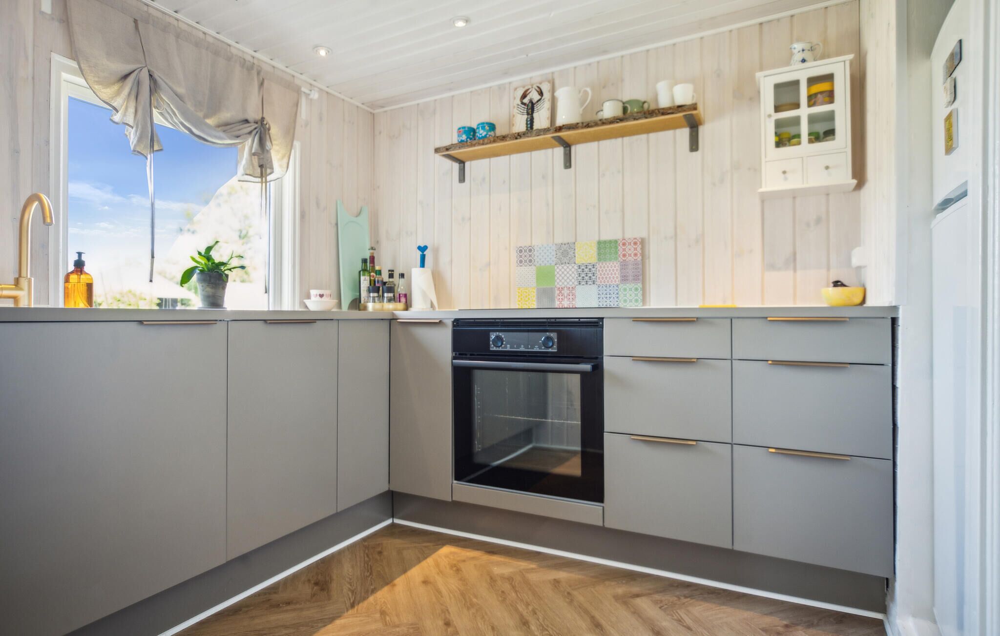 A modern kitchen with grey cabinets, a built-in oven, and a wooden floor.