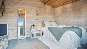 Ein gemütliches Schlafzimmer in einer Holzhütte mit Bett, Nachttisch und Spiegel.