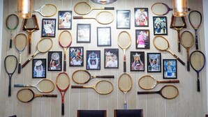 Una pared con diversas raquetas de tenis y fotografías enmarcadas de tenistas.