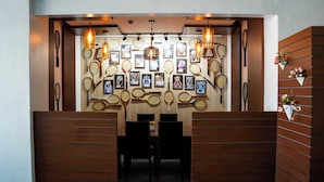 Una habitación con un muro decorado con marcos y cuadros, raquetas de tenis, paneles de madera y una mesa con sillas.