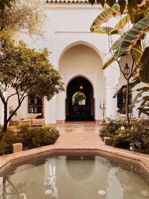 A courtyard with a pool, a seating area, and a view of a building through an arched doorway. - Riad Berbere Marrakech (Marrakech)