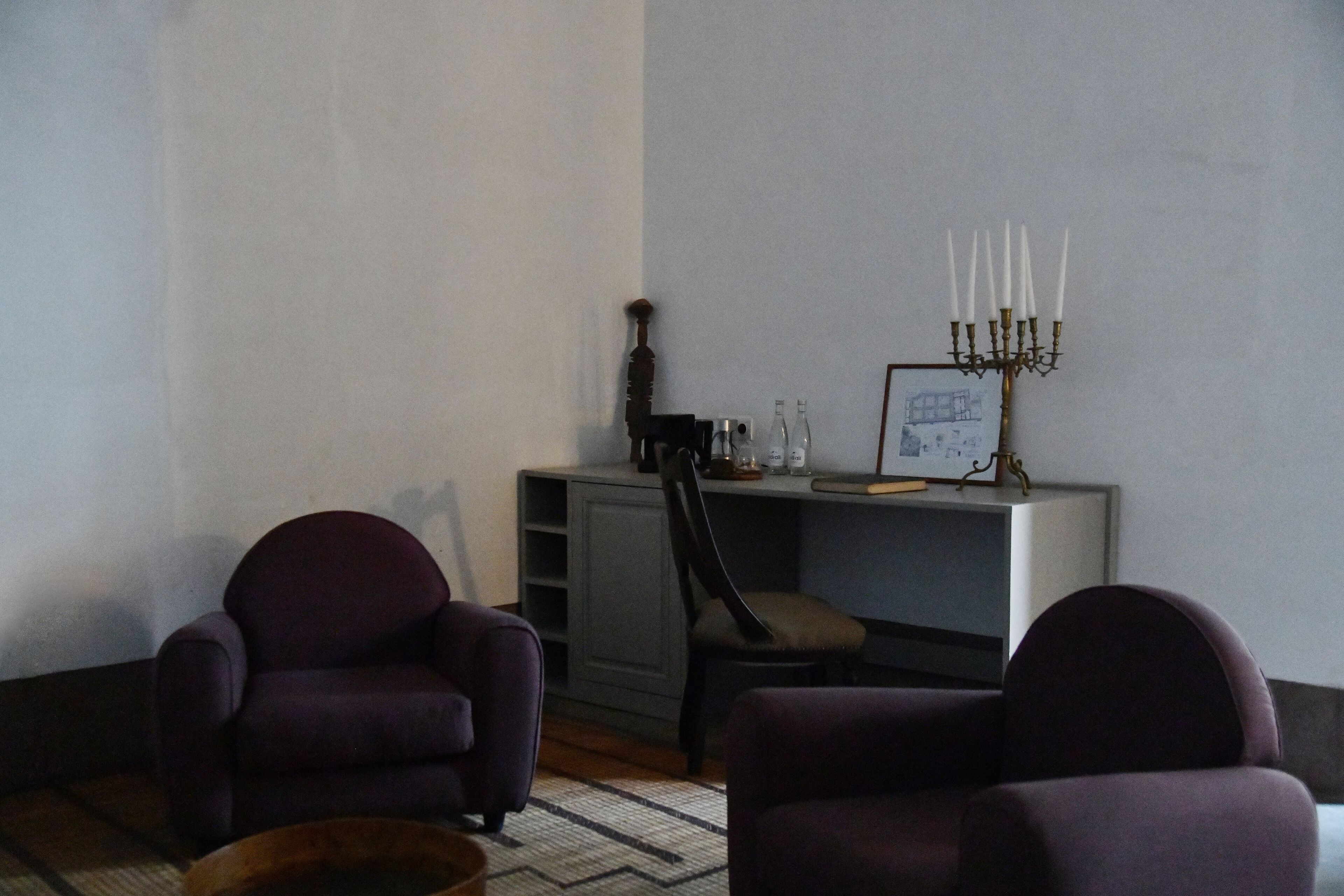 Una habitación con dos sillones morados, una mesita de madera, un candelabro con velas e imagen enmarcada sobre un mueble.