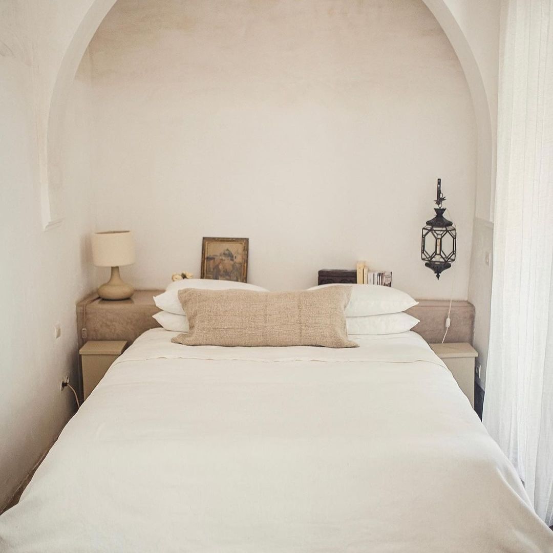 Une chambre à coucher avec un grand lit, une table de chevet avec une lampe, un cadre photo et un luminaire fixé au mur.
