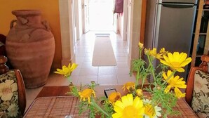 Et køkken med et køleskab, en stor vase med blomster og et spiseområde med et bord og stole.