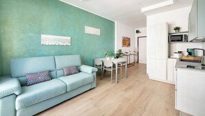 A modern living room with a light blue sofa, a dining table, and a kitchen area with white cabinets and a microwave. - Rome Experience (Rome)