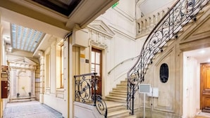 Una imponente escalera con barandales de metal ornamentados, piso de mármol y un techo alto con tragaluces.