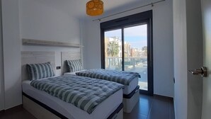 Ein Schlafzimmer mit zwei Betten, einem großen Fenster und Blick auf Gebäude.