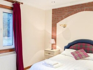 Een slaapkamer met een metselwerk open haard, een raam met uitzicht, een nachtkastje met een lamp, en een bed met kussens.