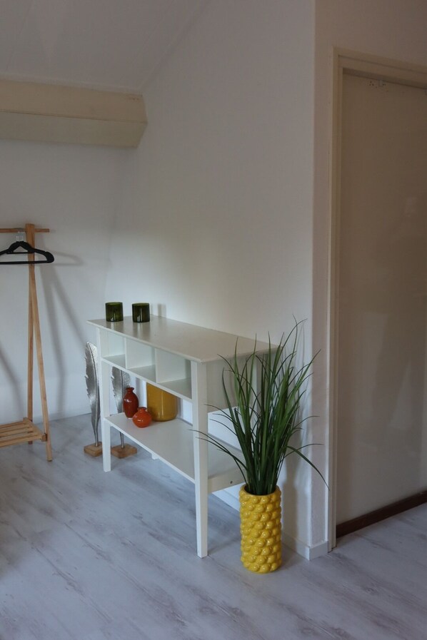 Una habitación blanca con un escritorio blanco, un caballete de madera y una maceta con forma de piña.