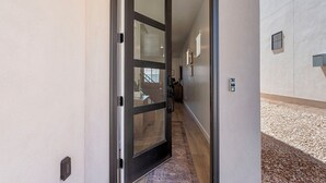 Un pasillo con una puerta de cristal que da a una habitación, suelo de madera y pared con textura.