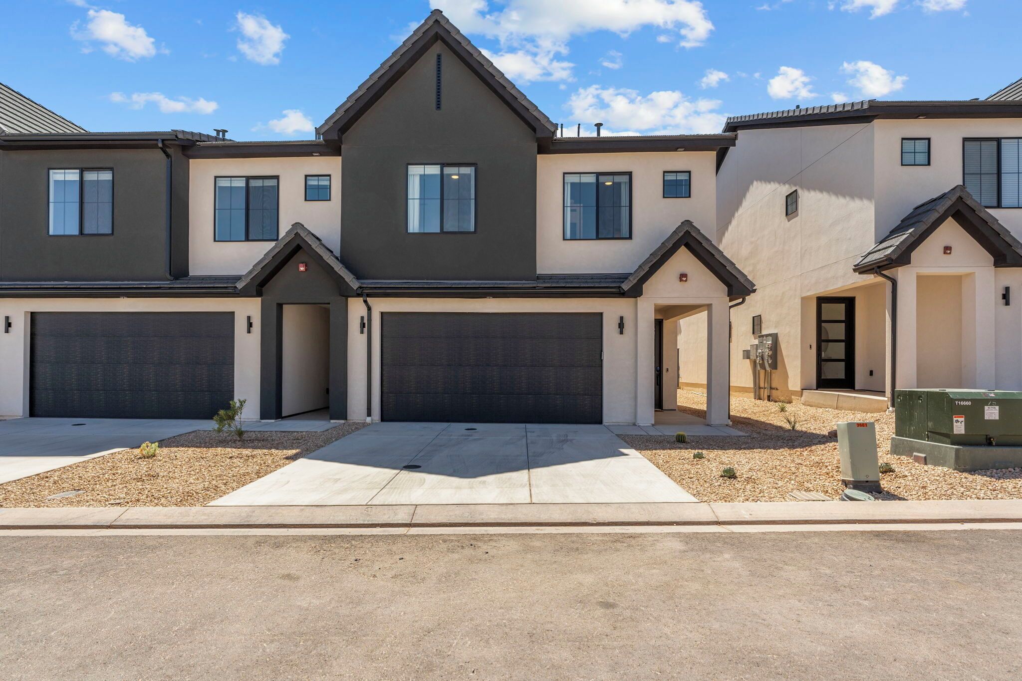 A modern two-story residential building with a garage entrance, a small landscaped area, and a utility box.