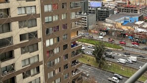 Un immeuble résidentiel à plusieurs étages, doté de balcons, offrant une vue sur une rue animée, avec des voitures et des travaux de construction, et sur les contours lointains de la ville.