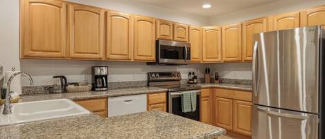 A kitchen with granite countertops, wooden cabinets, stainless steel appliances, and a dishwasher.