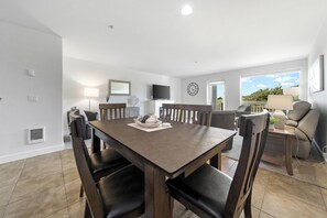 Un comedor con una mesa y sillas de madera, un televisor montado en la pared y un ventanal con vistas al verdor.