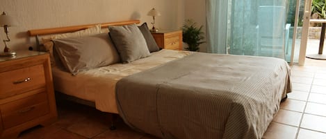 A bedroom with a bed, nightstands, a lamp, a potted plant, and a sliding glass door leading to an outdoor area.