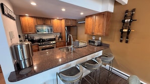 A modern kitchen with wooden cabinets, stainless steel appliances, and a bar area with stools.