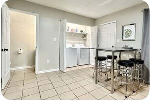 Una cocina con piso de baldosas, una zona con taburetes de bar y un refrigerador.