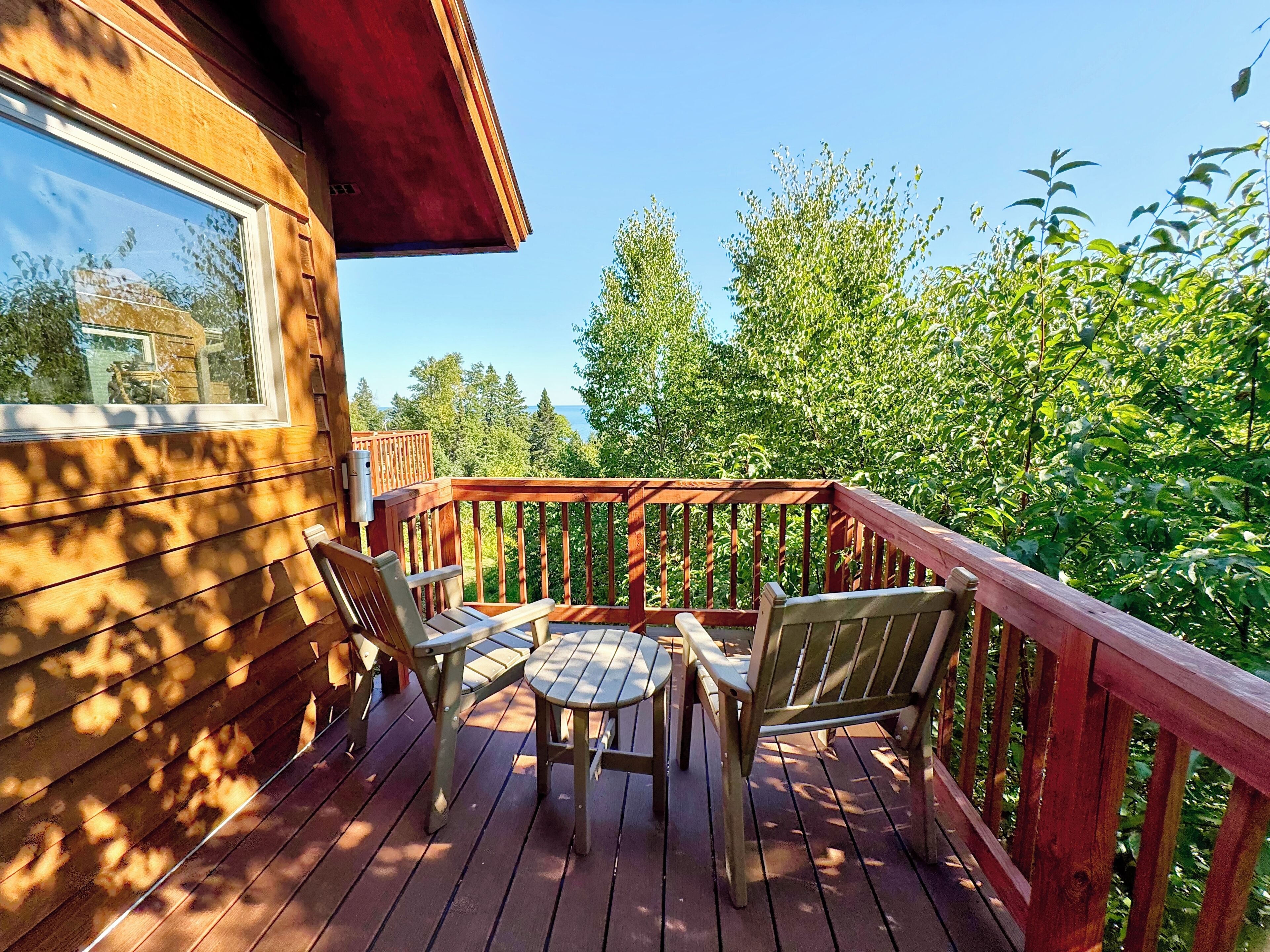 Eine Holzterrasse mit roter Geländer, einem Tisch und zwei Stühlen.