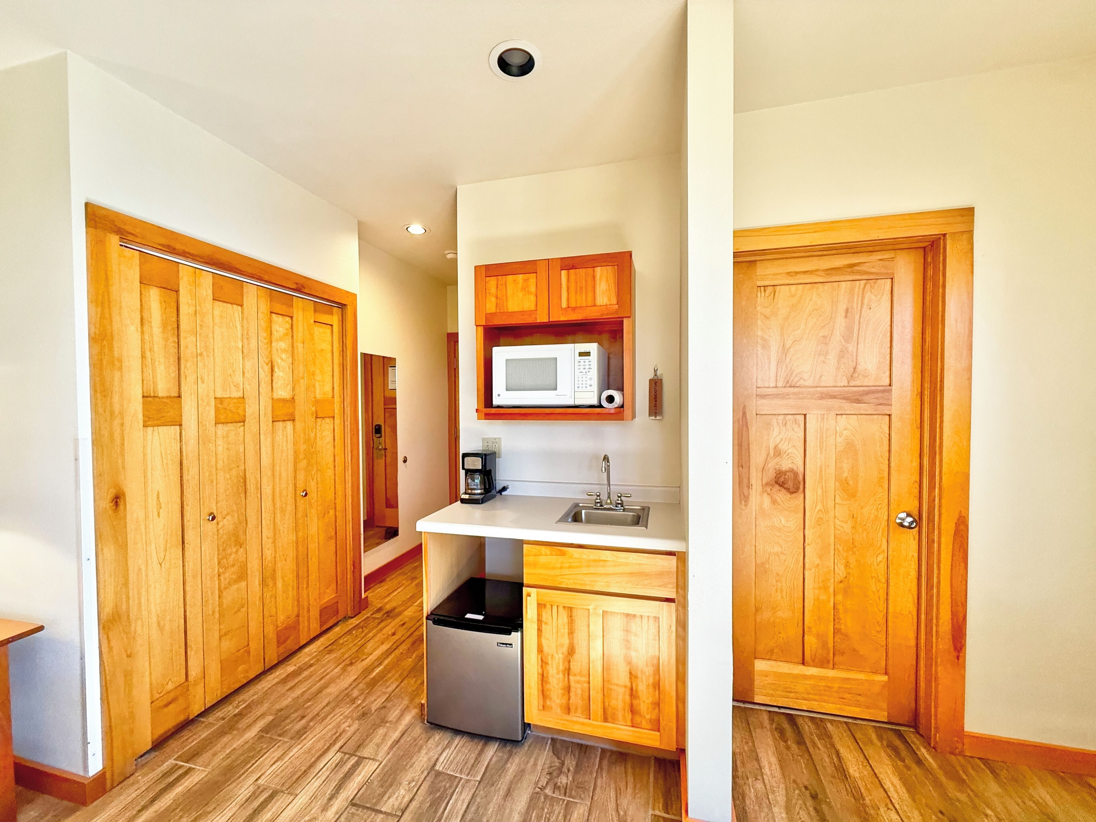 Cocina compacta con armarios de madera, microondas, cafetera y refrigerador pequeño.