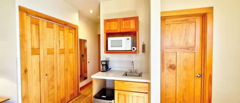 Cocina compacta con armarios de madera, microondas, cafetera y refrigerador pequeño.
