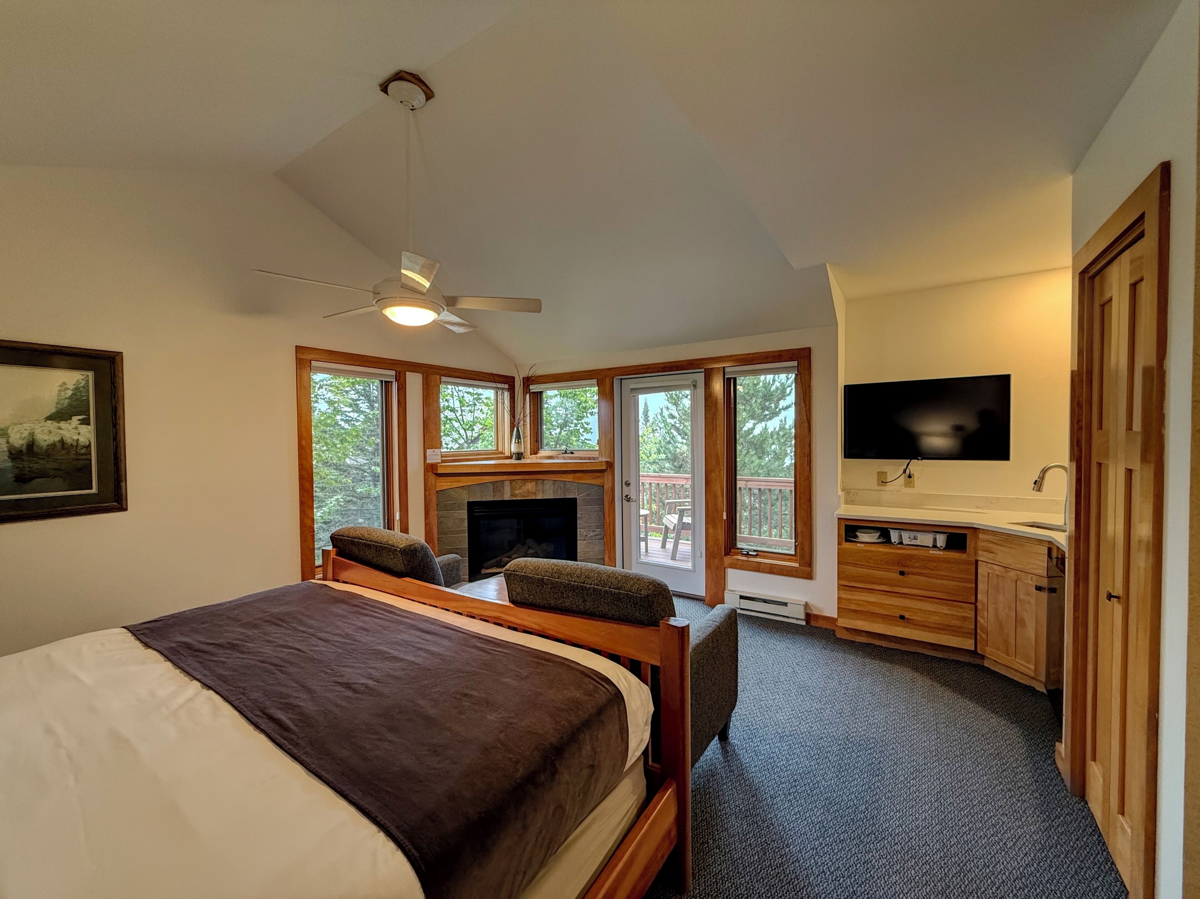 A bedroom with a bed, a fireplace, a TV, and a bathroom with a sink and mirror.
