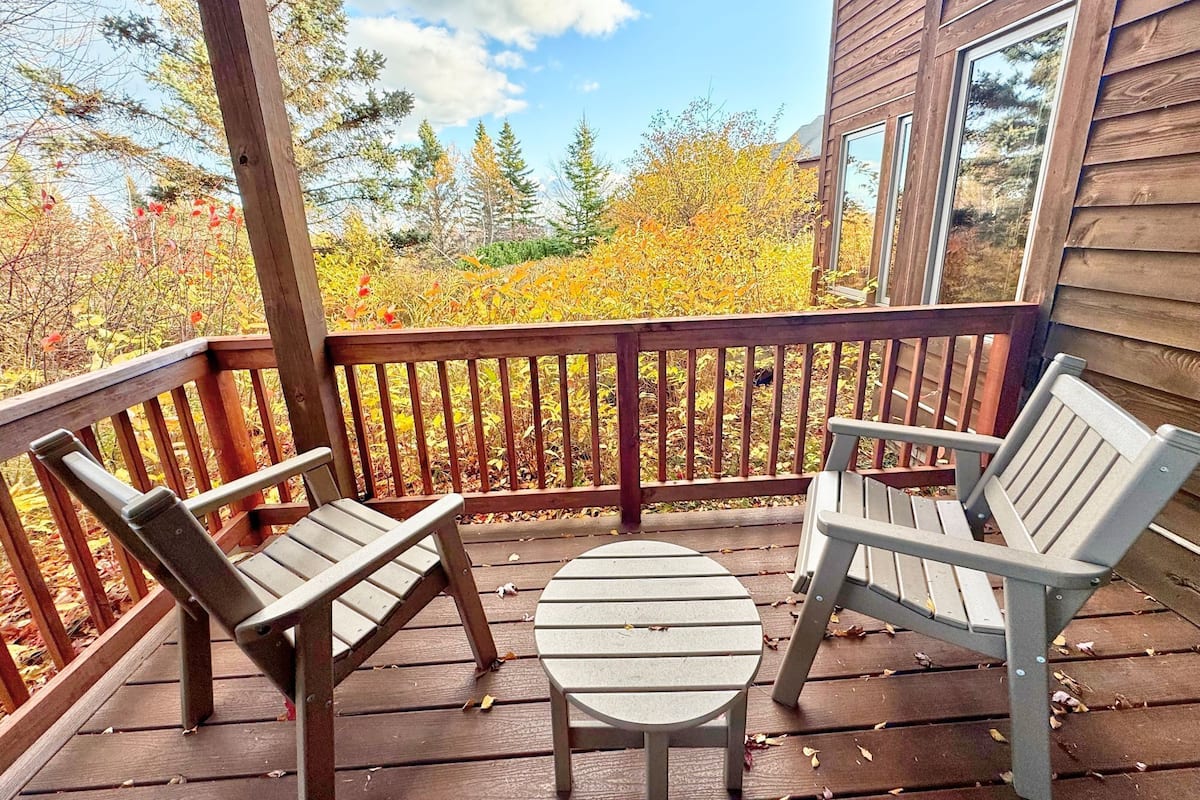 A wooden deck with two Adirondack chairs and a small round table.