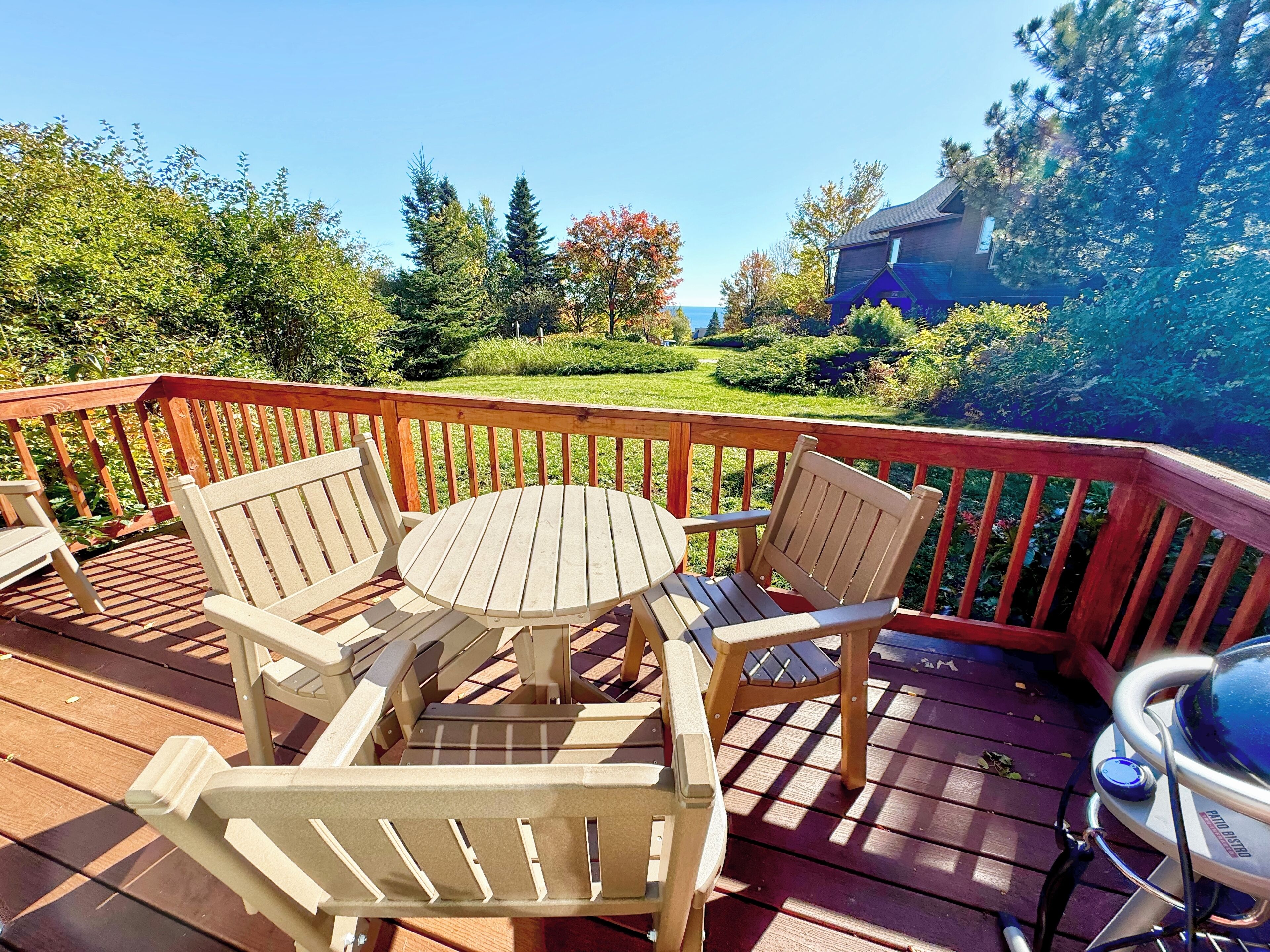A wooden deck with a round table and four chairs, surrounded by a wooden railing.