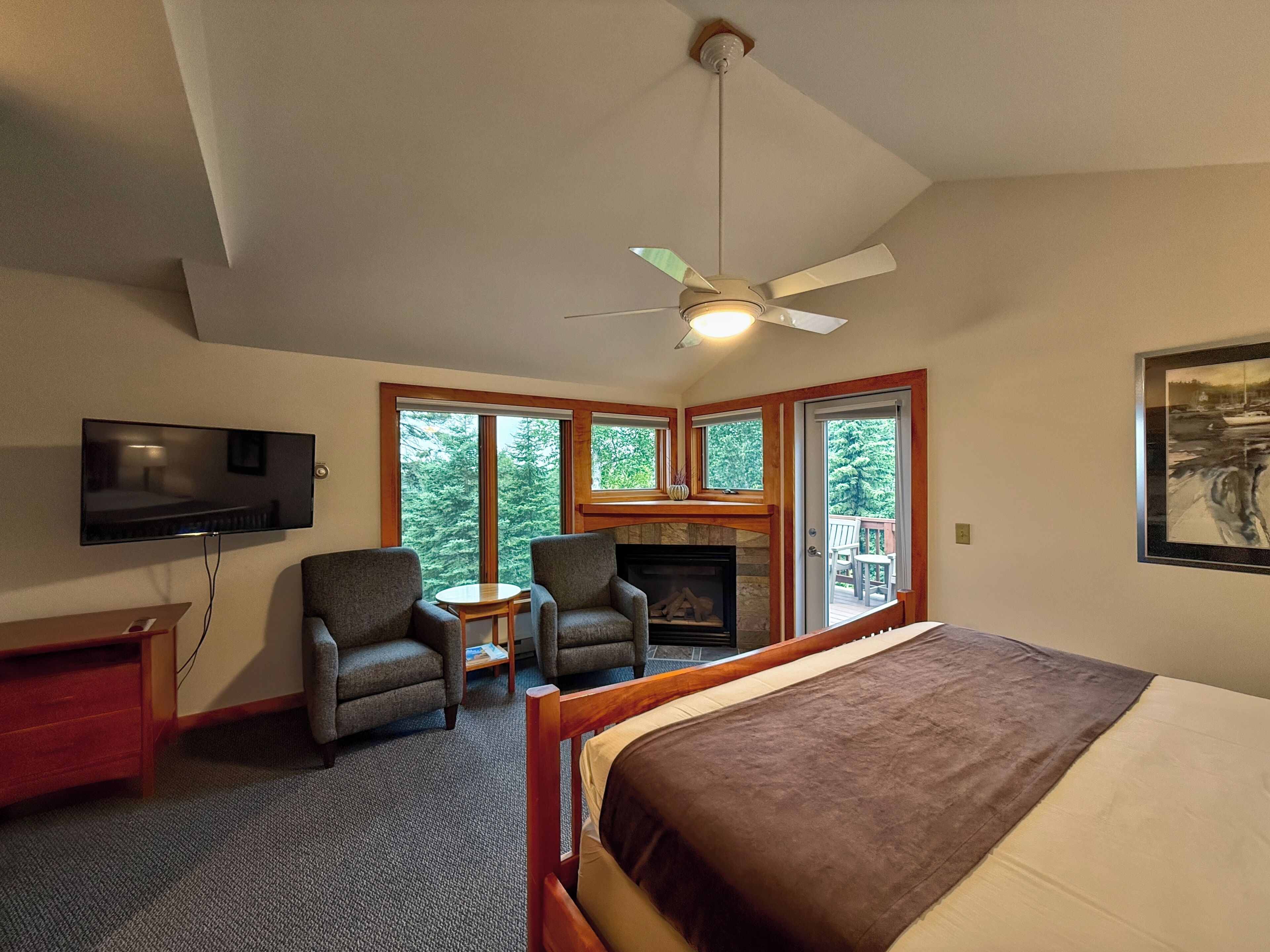 Une chambre à coucher comprenant un lit, un téléviseur, une cheminée, deux fauteuils, une petite table et un ventilateur de plafond.