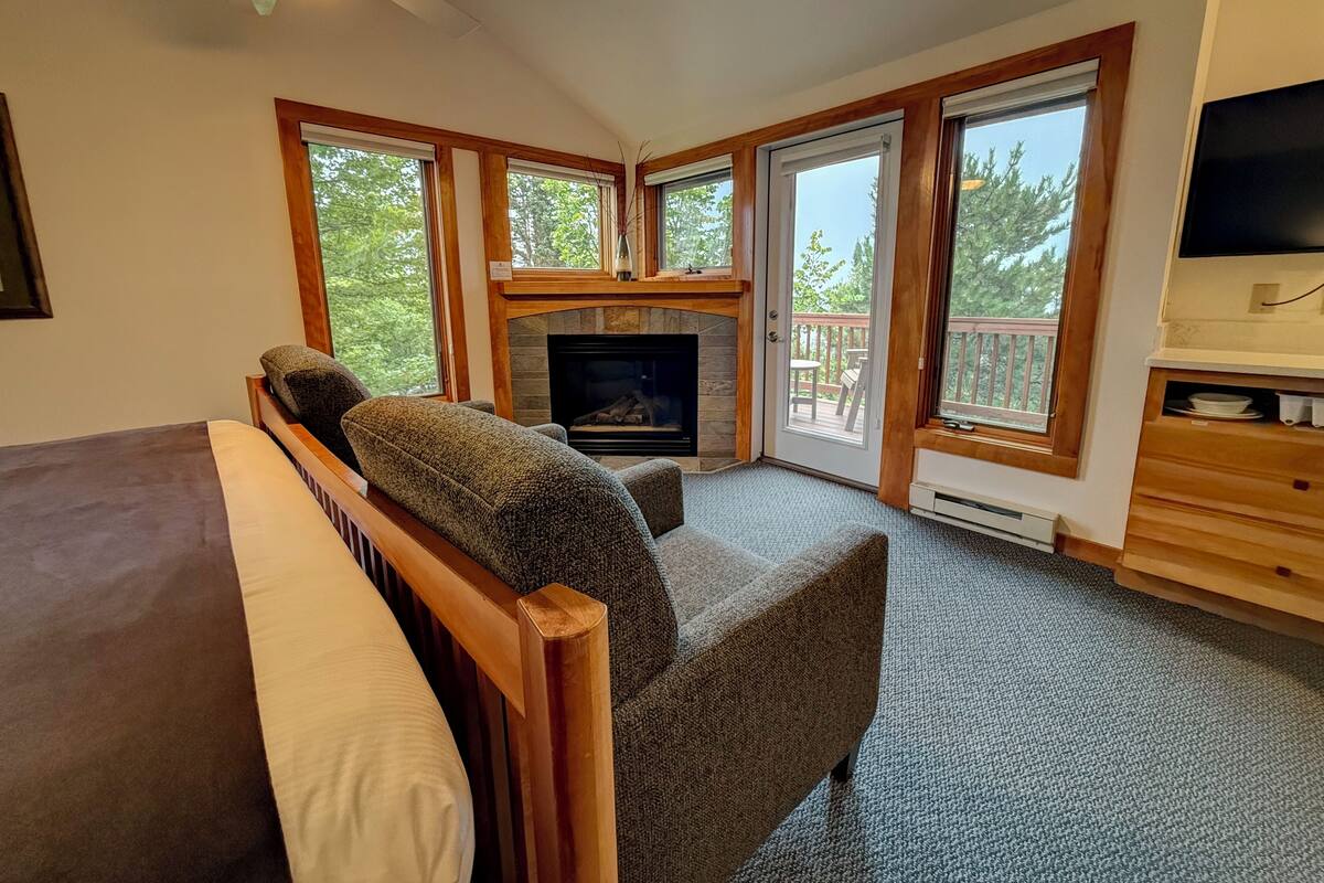 A cozy bedroom with a fireplace, a large window, and a television.
