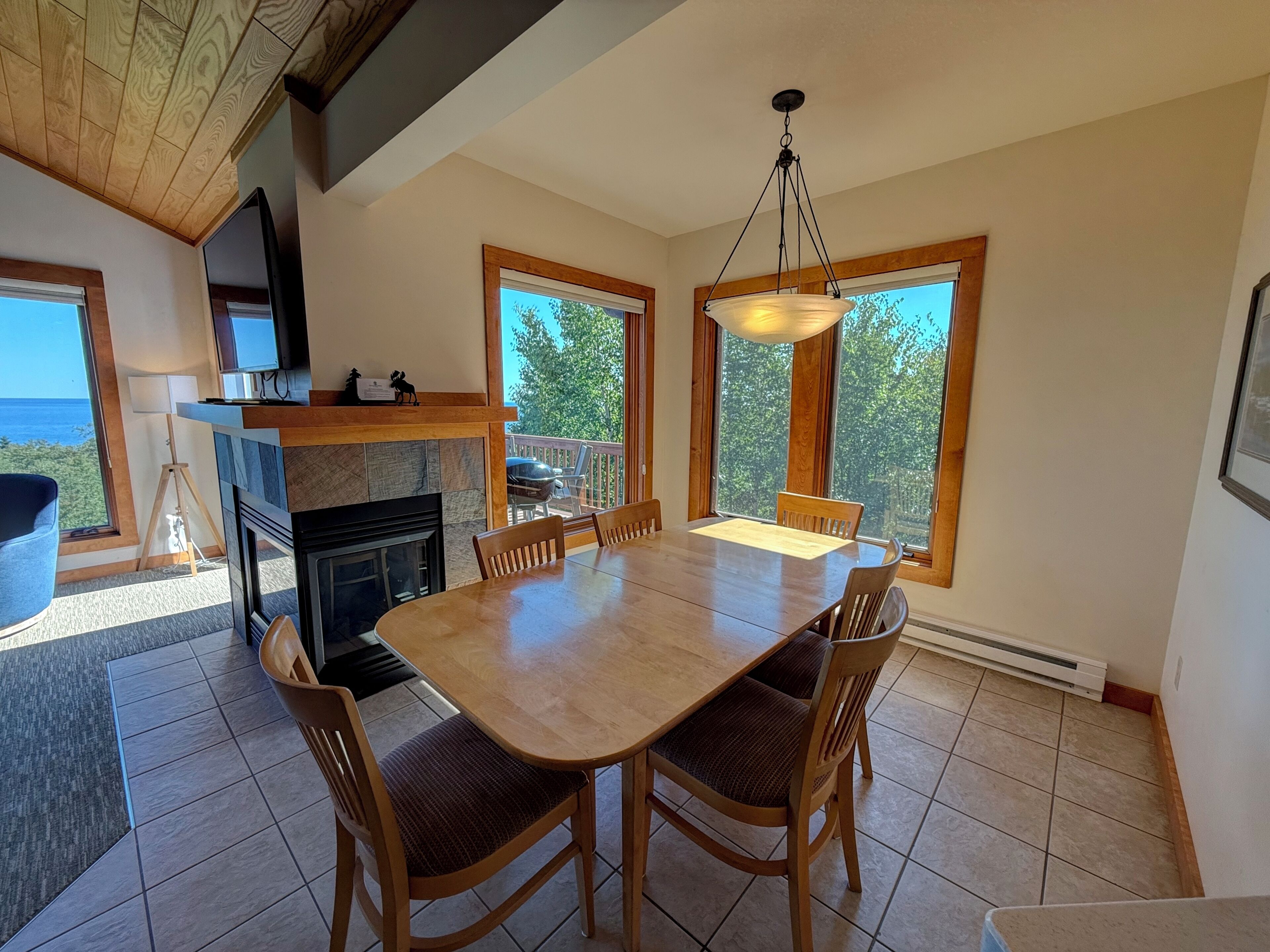 Un comedor con mesa y sillas de madera, una chimenea y ventanas amplias con vistas al exterior.