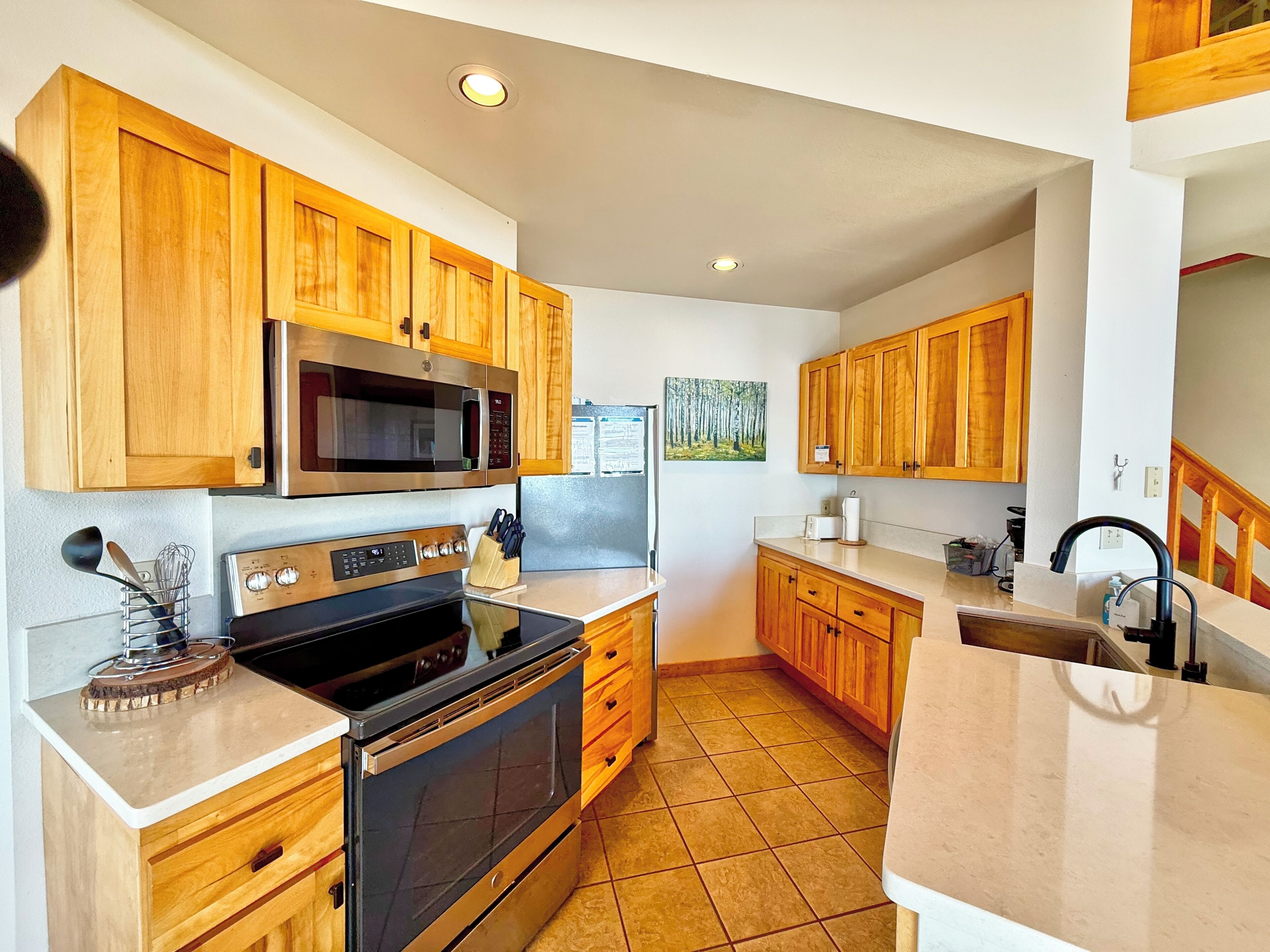 A modern kitchen with wooden cabinets, stainless steel appliances, and a tiled floor.