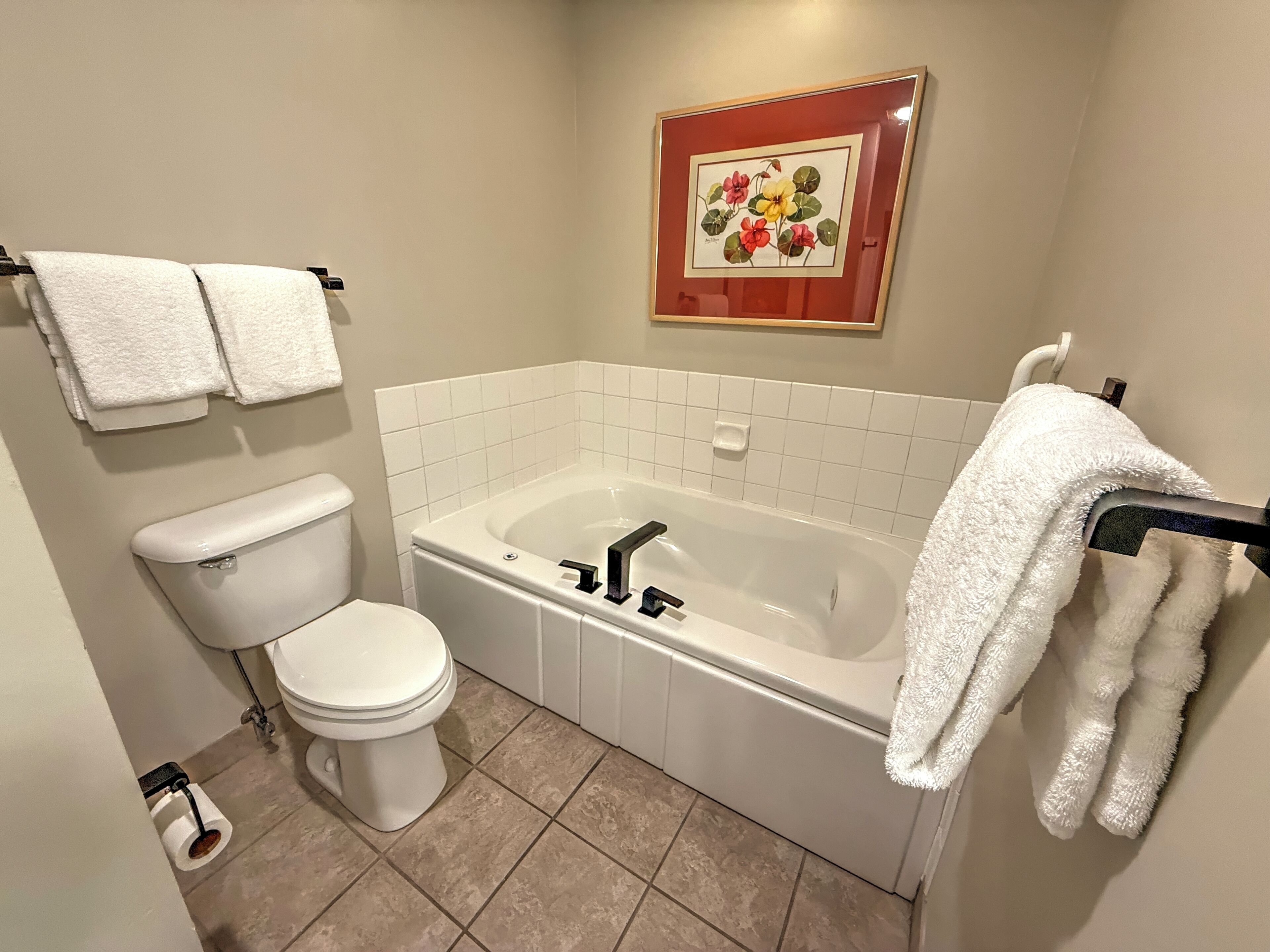 A bathroom with a toilet, a bathtub, and a framed floral artwork on the wall.