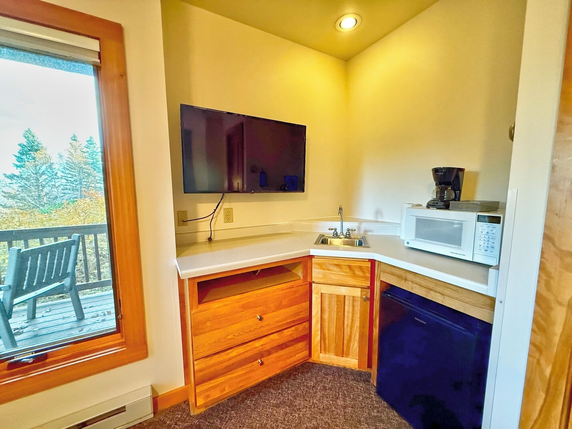 A compact kitchen with a microwave, coffee maker, and wooden cabinets.